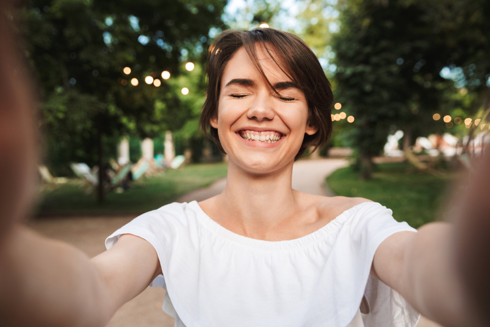 Cheerful young girl with eyes closeed taking a selfie at the park